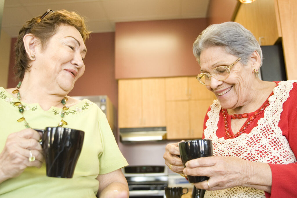 two seniors laugh while drinking coffee