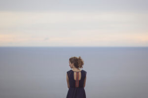 a young adult stands near a distant ocean