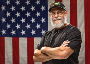 senior in front of a flag with a "Vietnam Veteran" hat