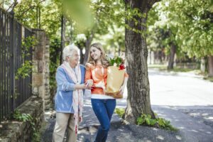 a young adult helps a senior walk down the street with groceries