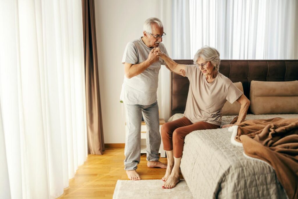 Man helps his wife out of bed after learning tips of how to support seniors after surgery