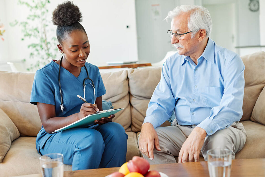 Health professional sits on couch next to senior and discusses medication management for aging adults